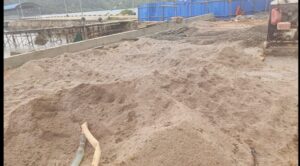 Penggunaan material pasir lokal yang bertumpuk di lokasi pembangunan proyek pelabuhan.