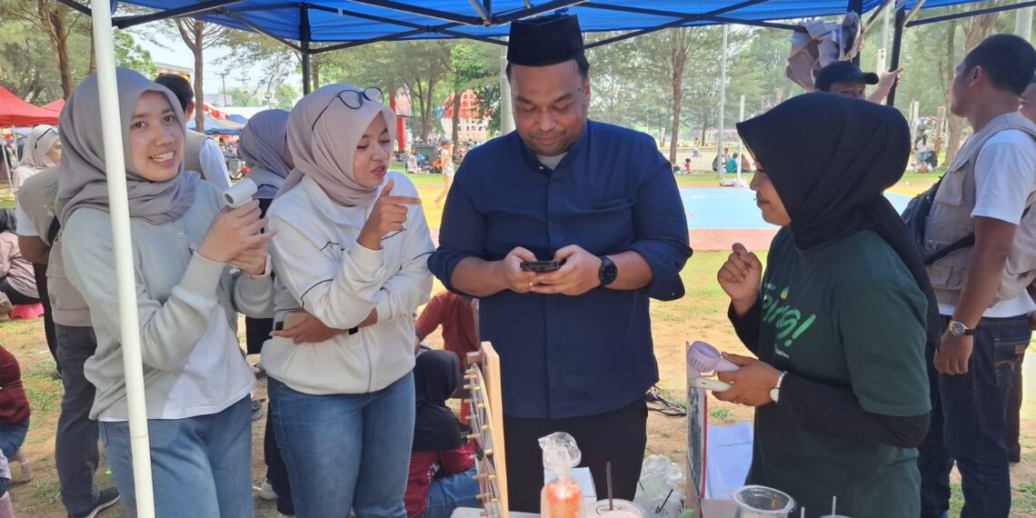 Kepala BPJS Ketenagakerjaan Kabupaten Natuna, Hendra Harry Jonna saat mendapatkan pelayanan para staf ketika melakukan top up tabungan emas digital melalui aplikasi tring! oleh PT. Pegadaian Cabang Natuna di lokasi booth pelayanan dan promosi aplikasi digital Tring! di Pantai Piwang yang di sejalanlan dengan kegiatan pawai budaya oleh Pemerintah Kabupaten Natuna dalam rangka kemeriahan HUT Natuna ke 27