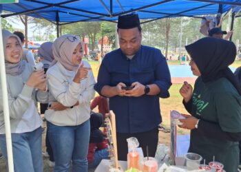 Kepala BPJS Ketenagakerjaan Kabupaten Natuna, Hendra Harry Jonna saat mendapatkan pelayanan para staf ketika melakukan top up tabungan emas digital melalui aplikasi tring! oleh PT. Pegadaian Cabang Natuna di lokasi booth pelayanan dan promosi aplikasi digital Tring! di Pantai Piwang yang di sejalanlan dengan kegiatan pawai budaya oleh Pemerintah Kabupaten Natuna dalam rangka kemeriahan HUT Natuna ke 27
